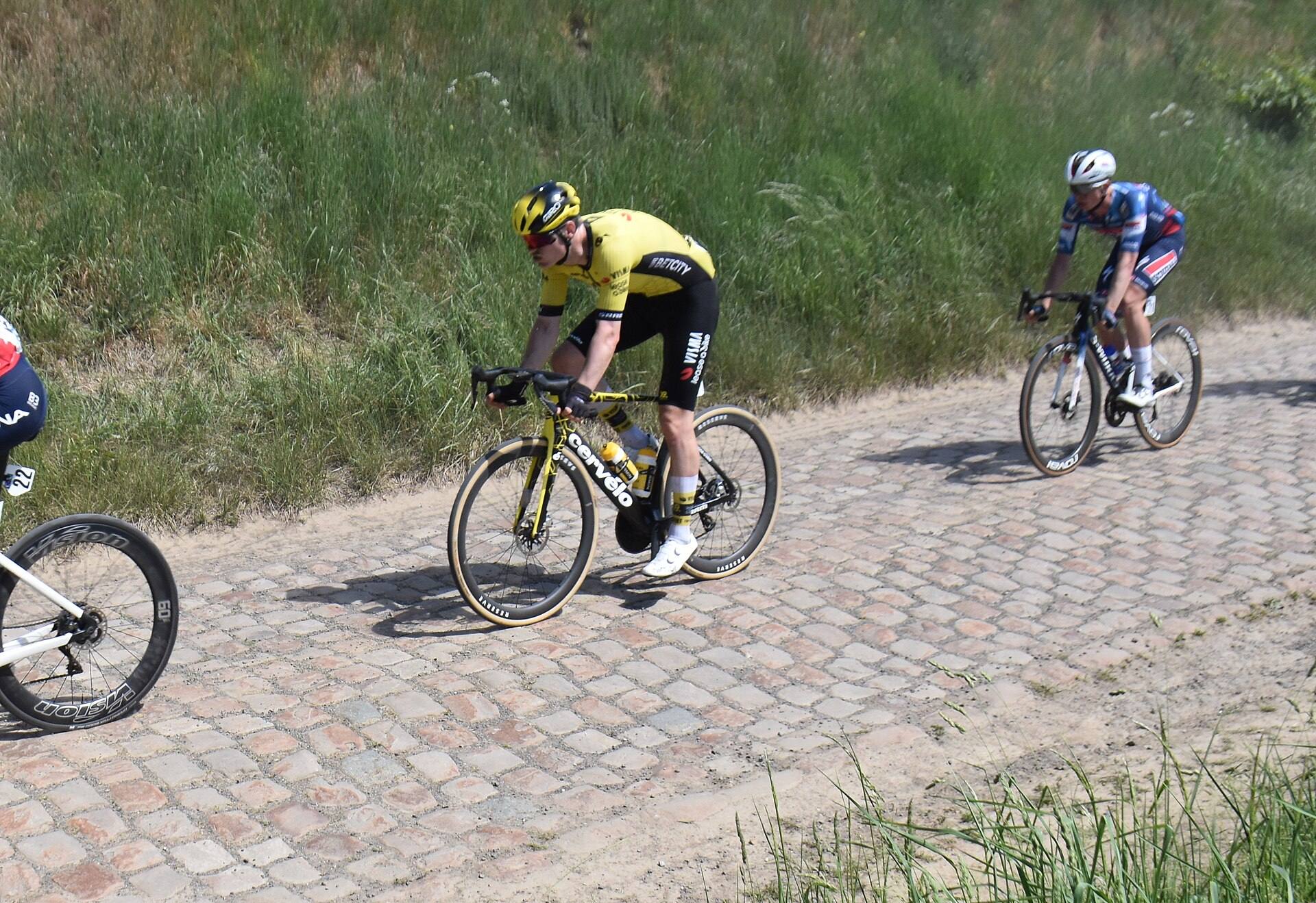 Trois coureurs sur un secteur pavé bordé d'herbe haute