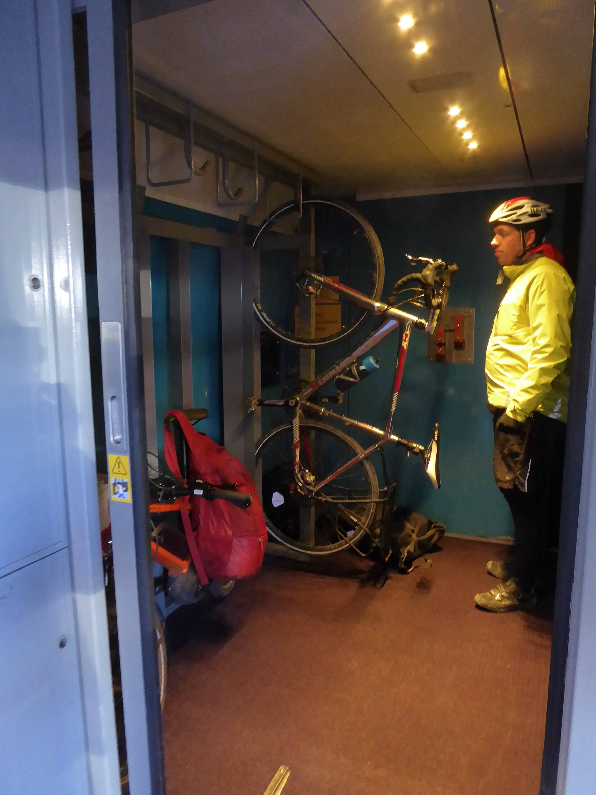 Vélo de route accroché verticalement dans l'emplacement vélo d'un TGV, son propriétaire debout à côté