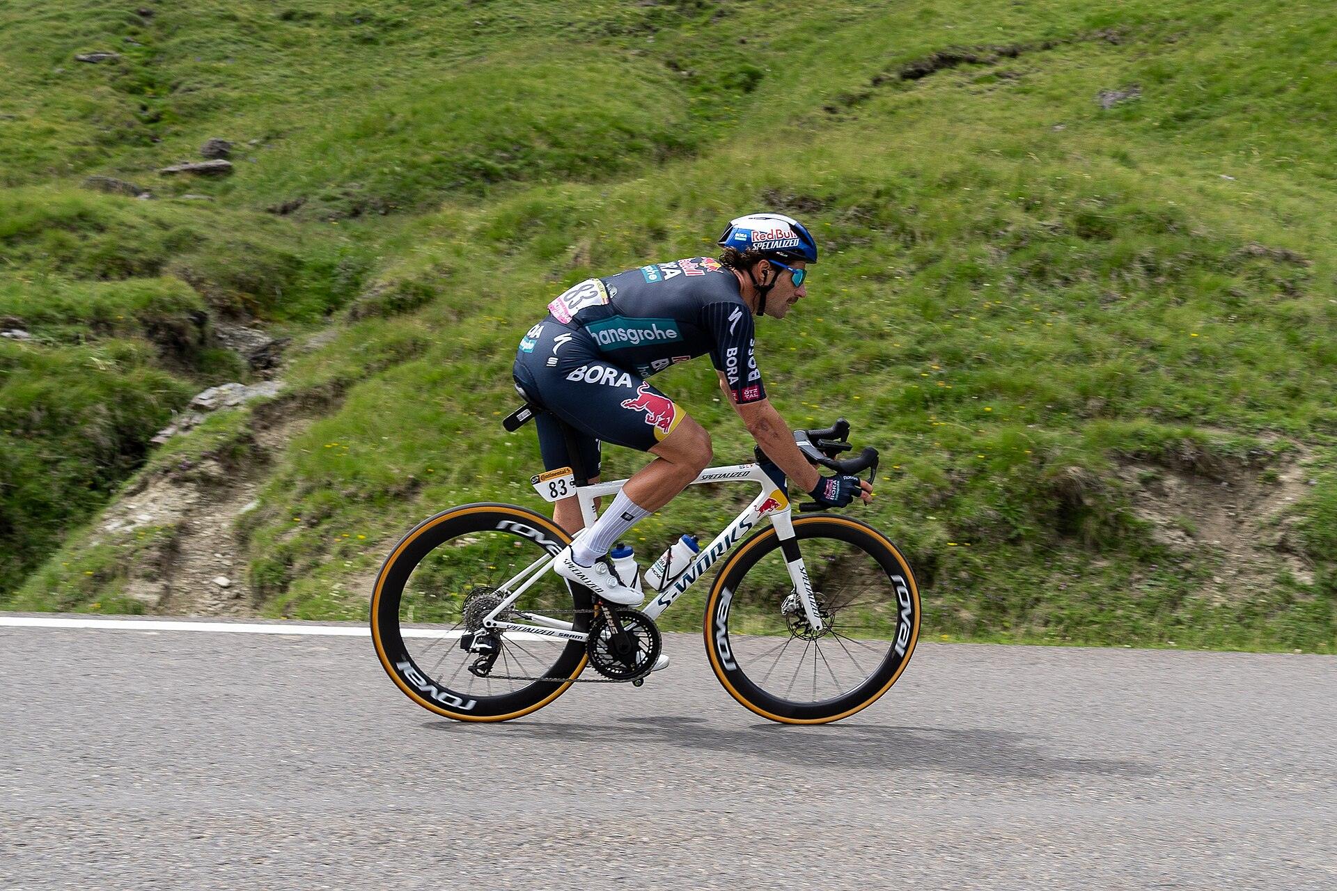 Coureur professionnel en position aérodynamique dans la descente du Tourmalet, pâturages en arrière-plan