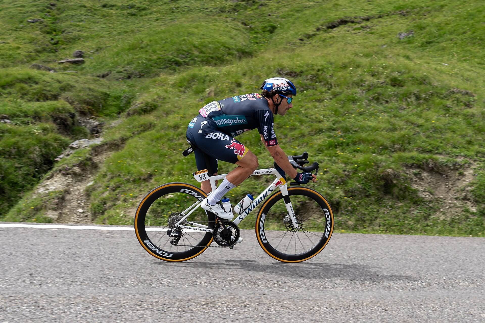 Coureur professionnel en position aérodynamique dans la descente du Tourmalet, pâturages en arrière-plan